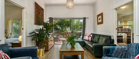 A spacious living room with a wooden coffee table, black leather sofas, and a large window offering a view of the outdoors.