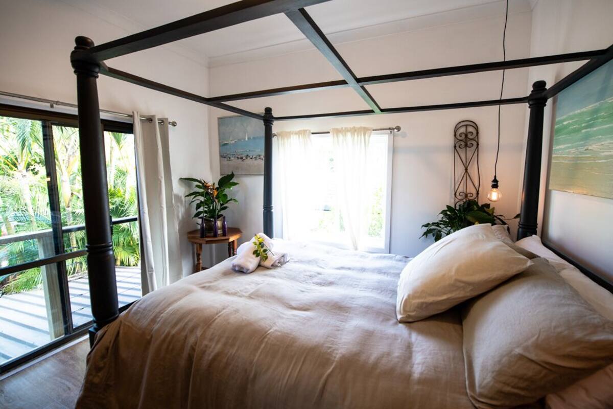 Ein Himmelbett mit Blick auf Palmen durch große Fenster.