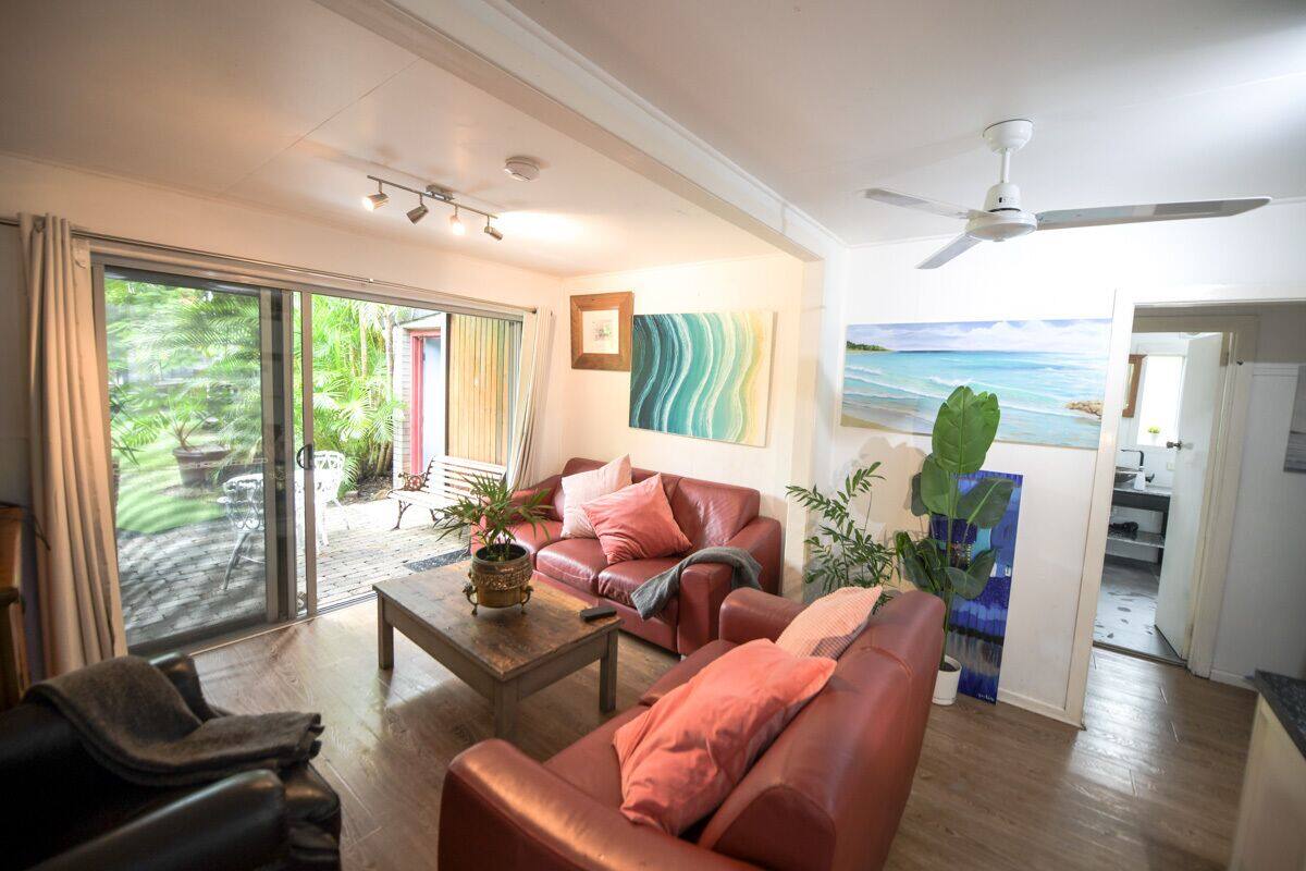Ein geräumiges Wohnzimmer mit großen Schiebeglastüren, die auf eine Terrasse führen, einem Deckenventilator und Meerblick durch ein großes Fenster.