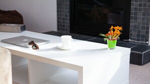 Une table blanche avec un ordinateur portable, une tasse blanche et un vase vert contenant des fleurs.