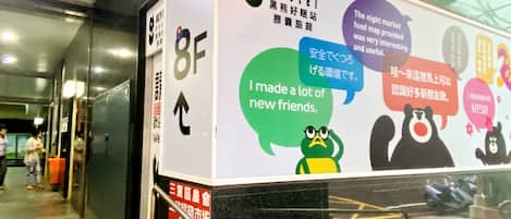 Un pasillo con un letrero del 'HeyBear Hostel' que presenta un personaje de oso y texto sobre conocer gente nueva.