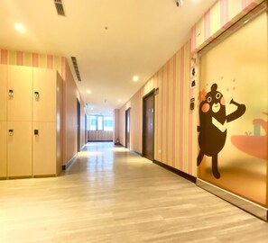 A hotel corridor with lockers, a striped wall, and a cartoon character decoration. - Heybear Capsule Hotel (New Taipei City)