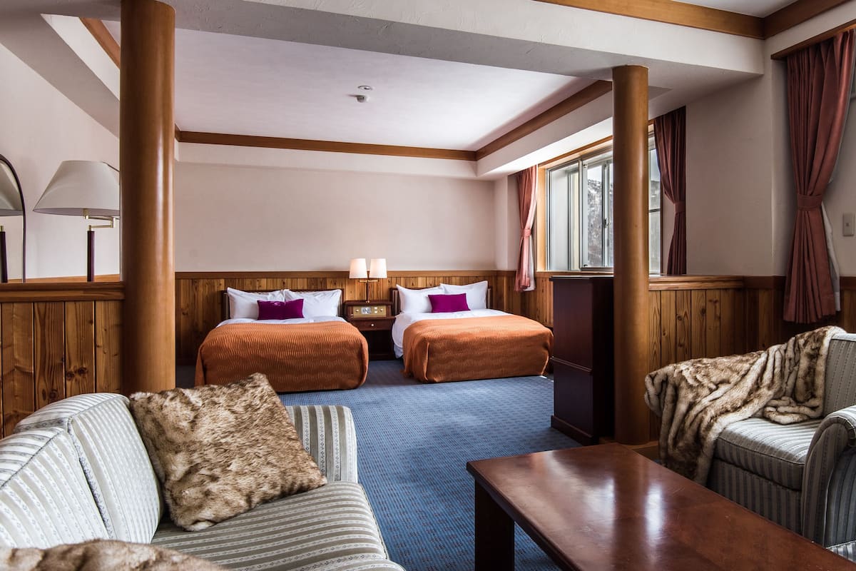 A hotel room with two beds, a sofa, a coffee table, and a view of a mountainous landscape.