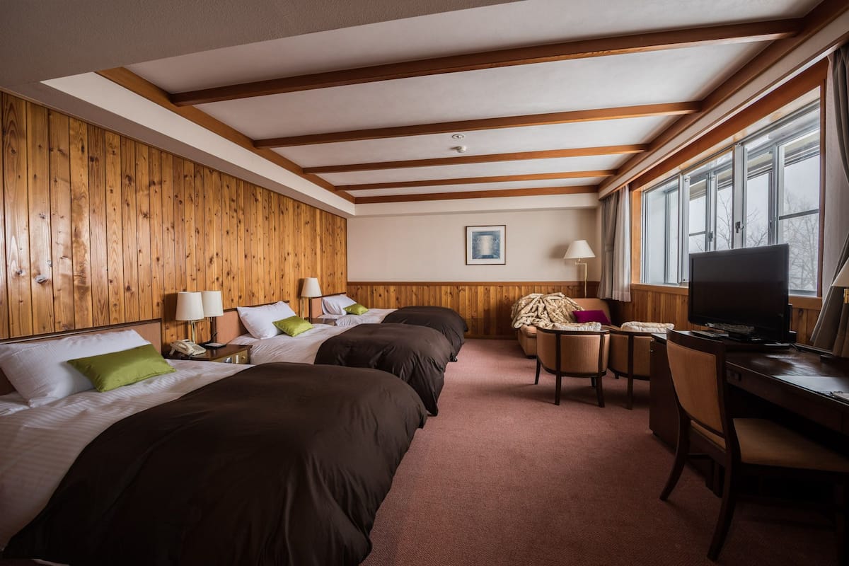 A hotel room with three beds, a desk with a television, and a window with curtains.