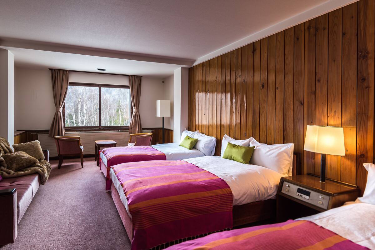 A hotel room with two beds, a desk, a chair, and a window with curtains.