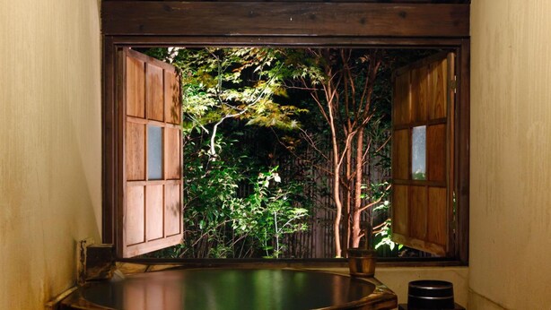 A traditional Japanese-style room with a wooden bathtub, a window with wooden shutters, and a view of a lush garden. - Sozankyo (Aso)