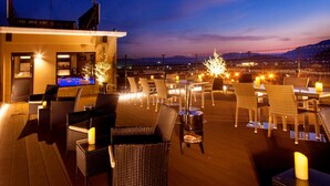 A rooftop terrace with wicker furniture, candles, and a view of the cityscape at dusk. - Sozankyo (Aso)