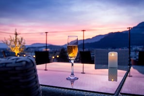 A glass of wine on a table with a candle, overlooking a scenic view of mountains and a sunset. - Sozankyo (Aso)