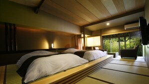 A traditional Japanese-style room with tatami mats, a low wooden bed, and a view of greenery through large windows. - Sozankyo (Aso)