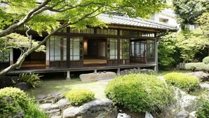 A traditional Japanese-style building with a wooden exterior, large windows, and a garden with rocks and greenery. - Sozankyo (Aso)