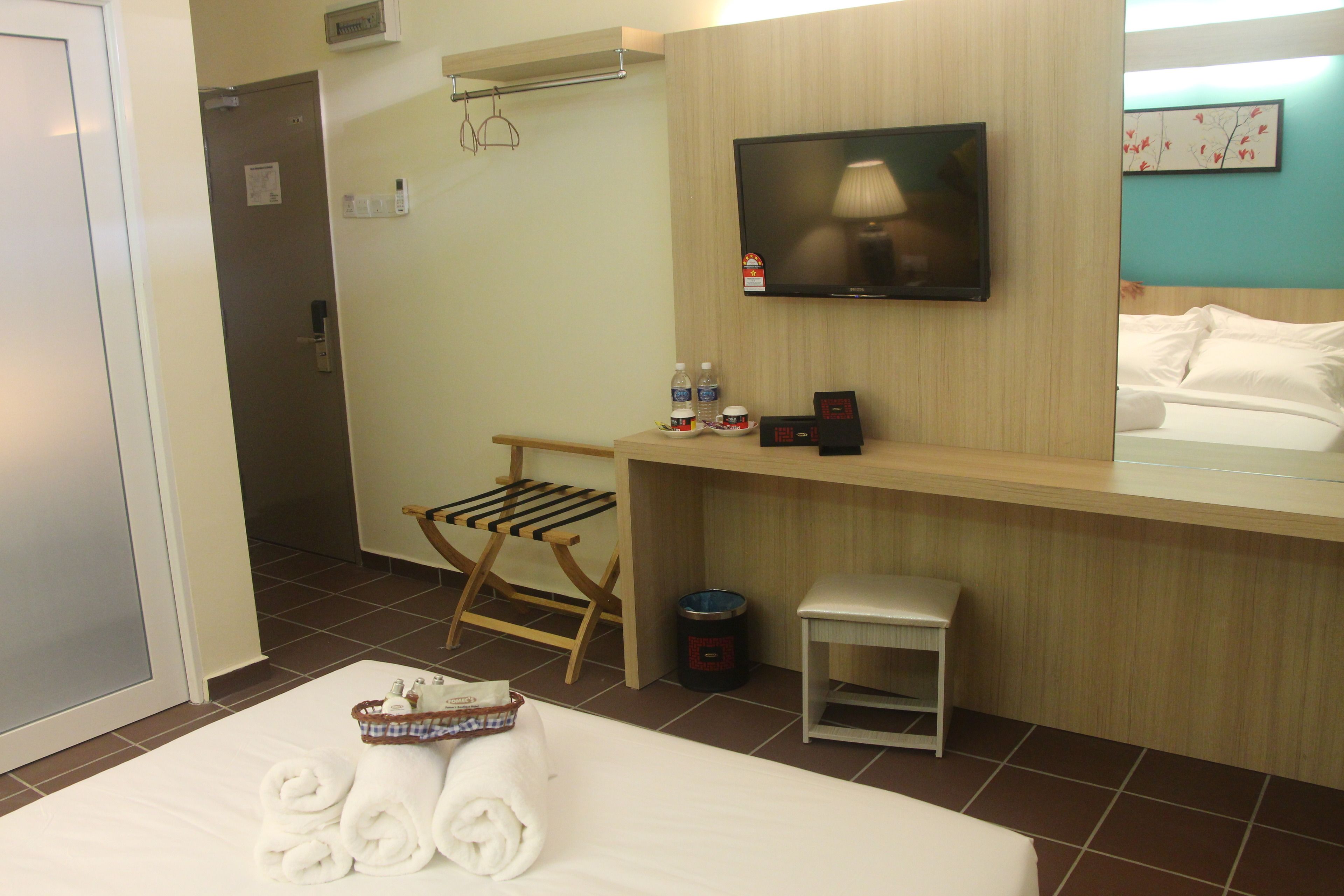 Ein Hotelzimmer mit Bett, Wandfernseher, kleinem Tisch, Stuhl und Mülleimer.