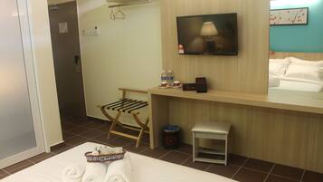 Ein Hotelzimmer mit Bett, Wandfernseher, kleinem Tisch, Stuhl und Mülleimer.