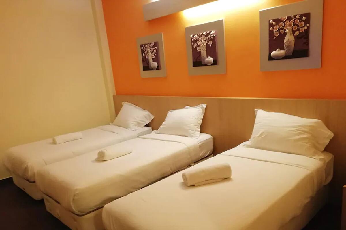 Une chambre d’hôtel avec deux lits simples, chacun agrémenté de draps et d’oreillers blancs, ainsi que d’une tête de lit. Trois tableaux encadrés représentant des motifs floraux sont accrochés au mur orange, au-dessus des lits.