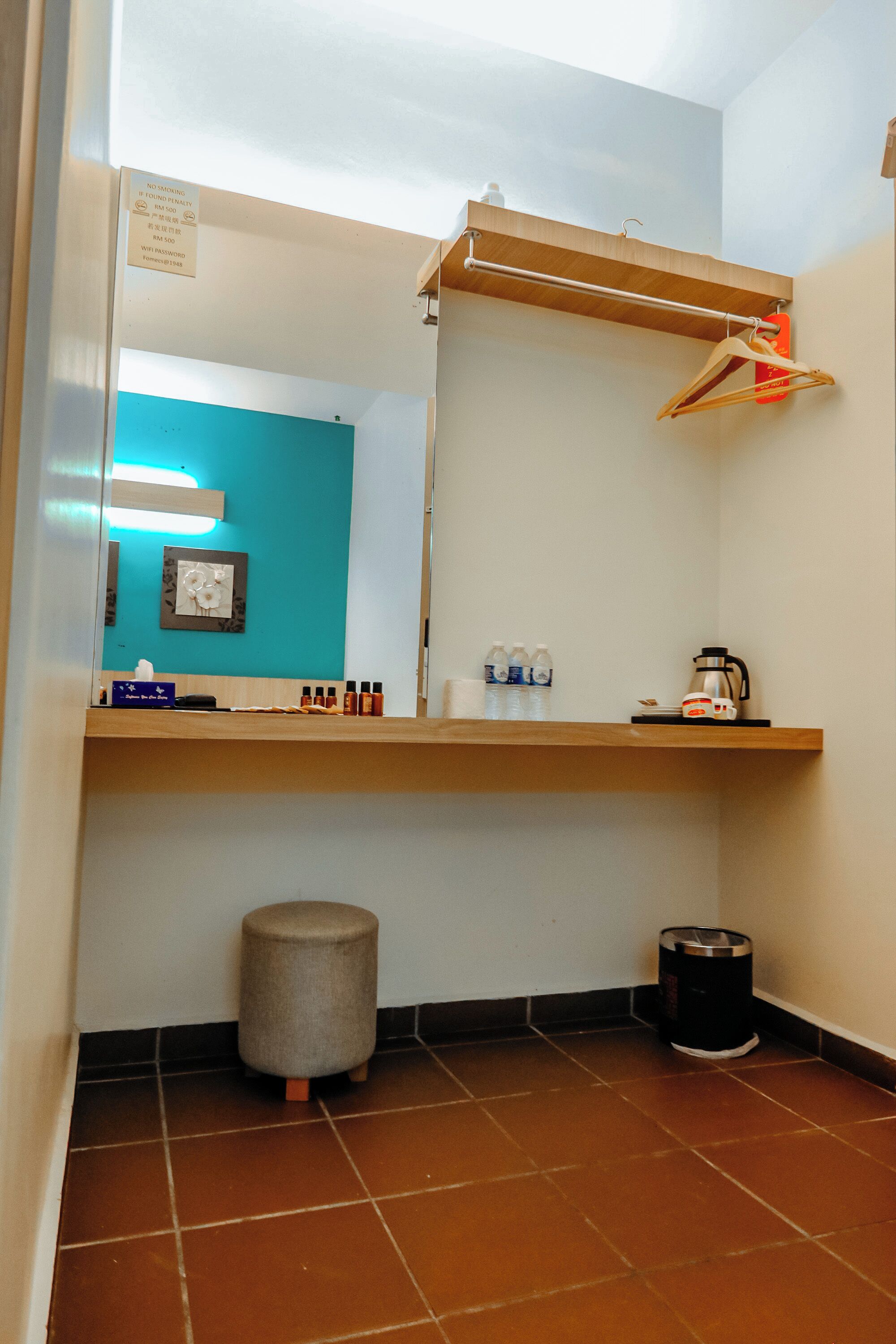 A small bathroom with a mirror, a towel rack, a sink, a trash can, and a shelf with toiletries.