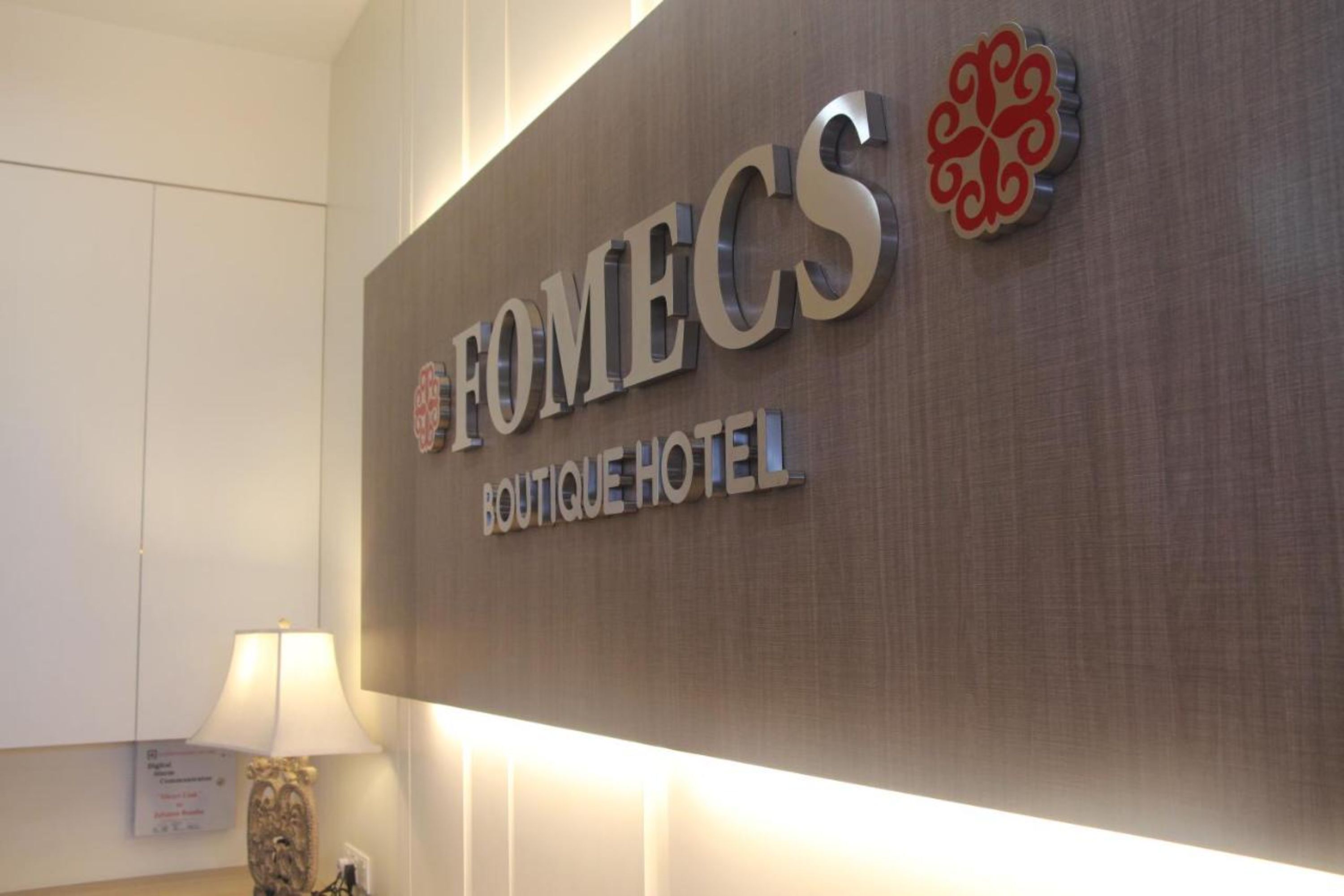 A sign for the Fomecs Boutique Hotel with a modern design and a decorative emblem.