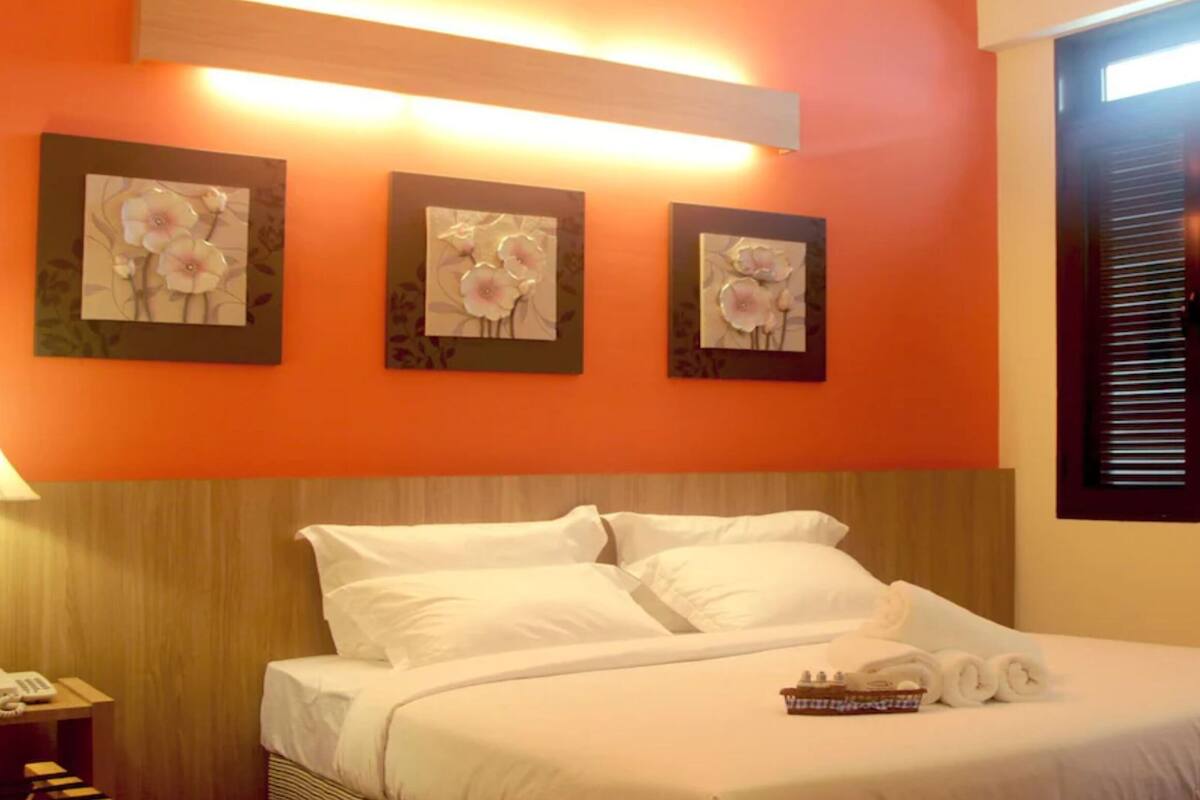 Une chambre d’hôtel avec un lit, une table de chevet avec une lampe et trois œuvres d’art florales encadrées accrochées au mur.