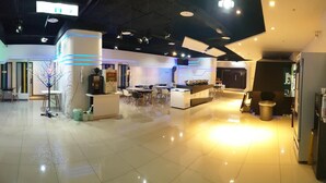 A modern hotel lobby with a central reception desk, seating areas, and a large screen.