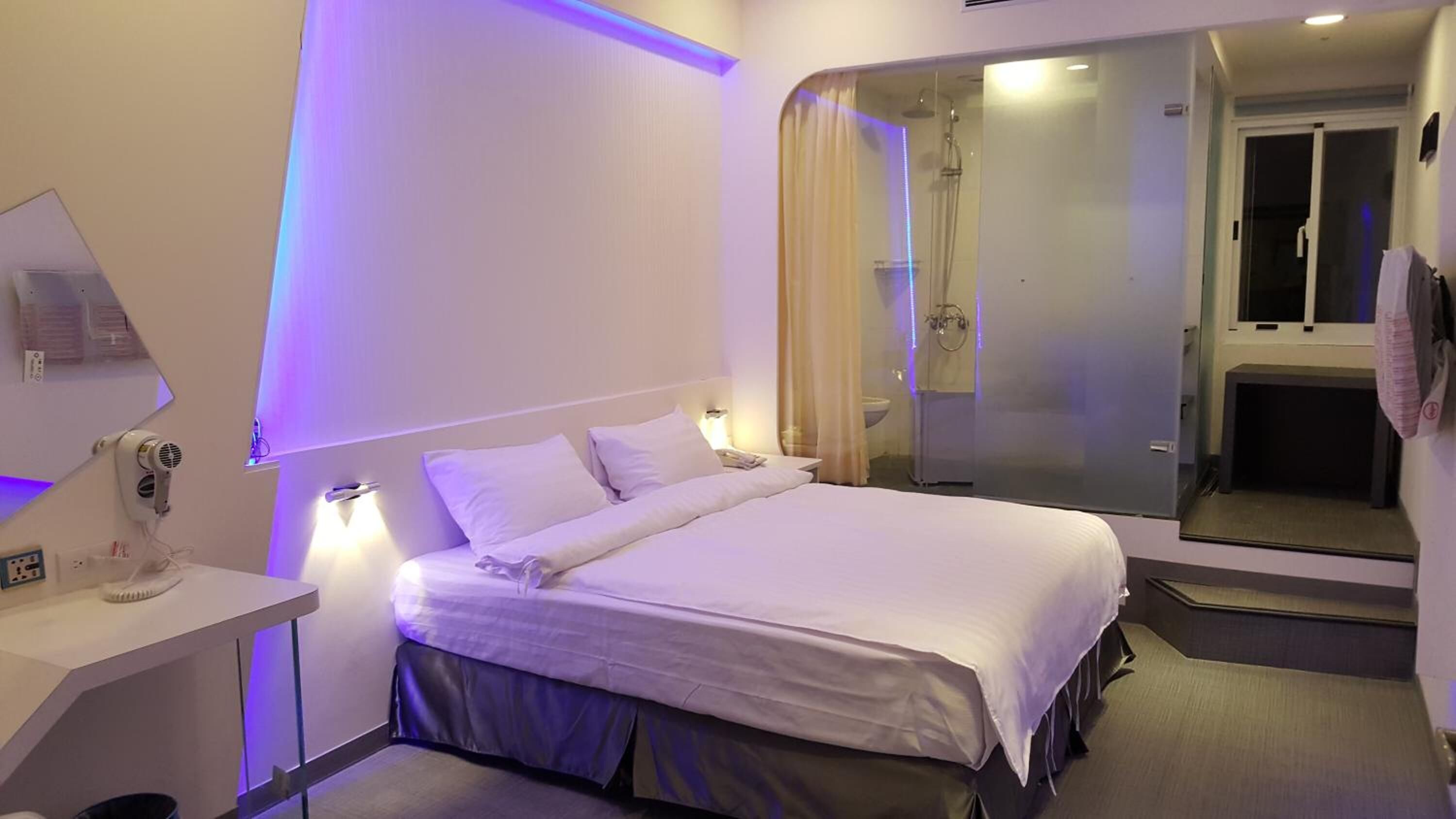 A modern hotel room with a large bed, bedside tables, a mirror, and a shower area.