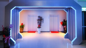 A modern hotel lobby with a geometric entrance, potted plants, and a clean, reflective floor.