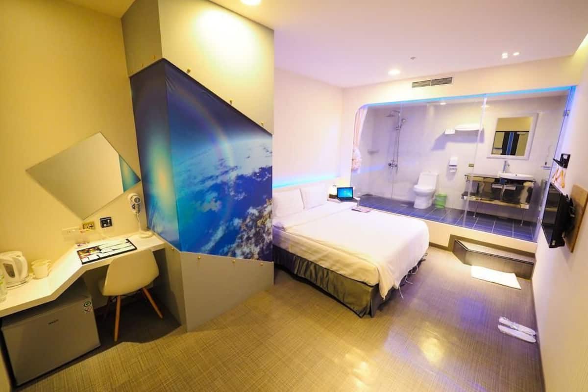 A hotel room with a bed, desk, and shower area.