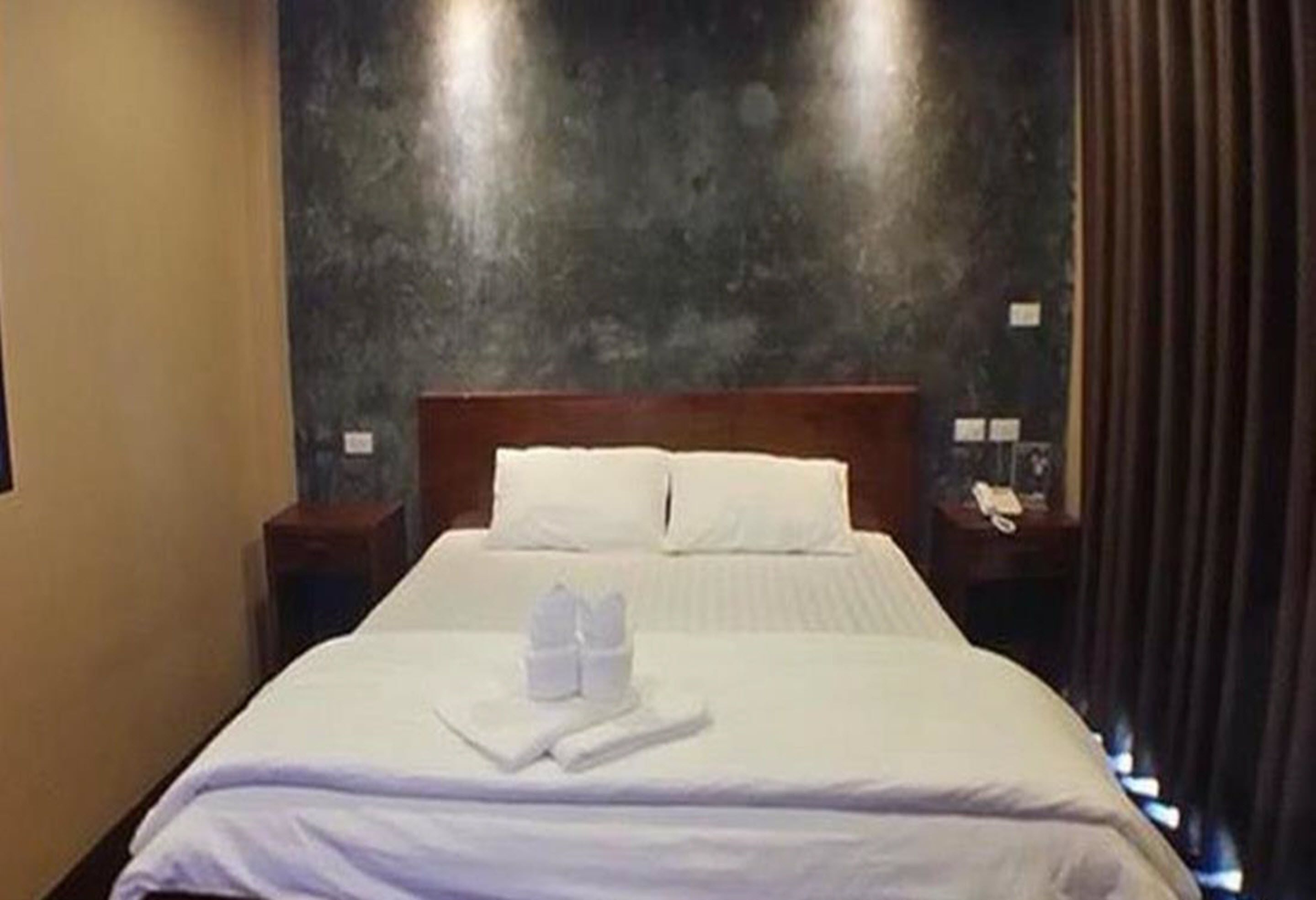 A neatly made bed with white linens and towels, a wooden headboard, and a dark textured wall behind it.