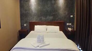 A neatly made bed with white linens and towels, a wooden headboard, and a dark textured wall behind it.