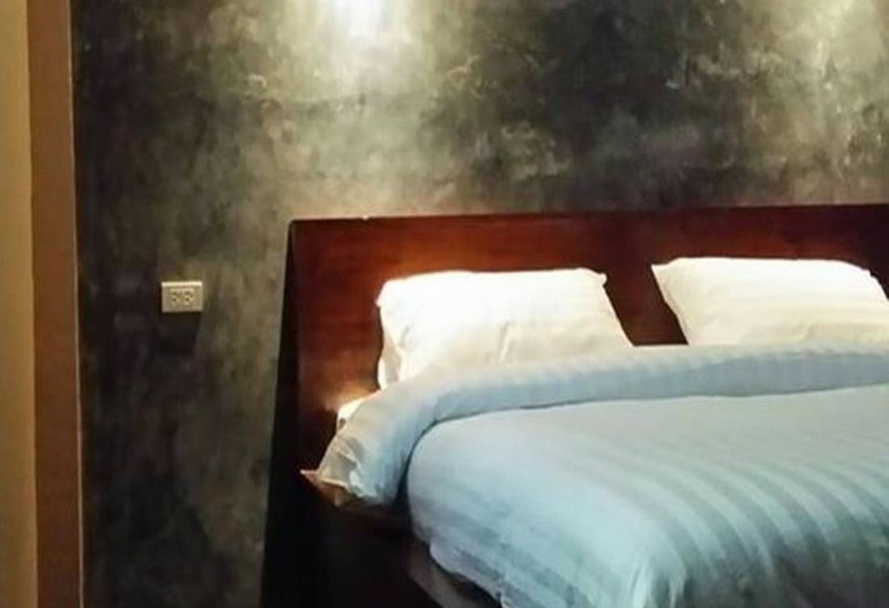 A bed with white and blue bedding, a wooden headboard, and a textured wall behind it.