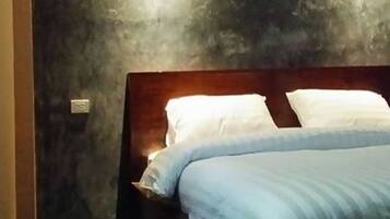 A bed with white and blue bedding, a wooden headboard, and a textured wall behind it.