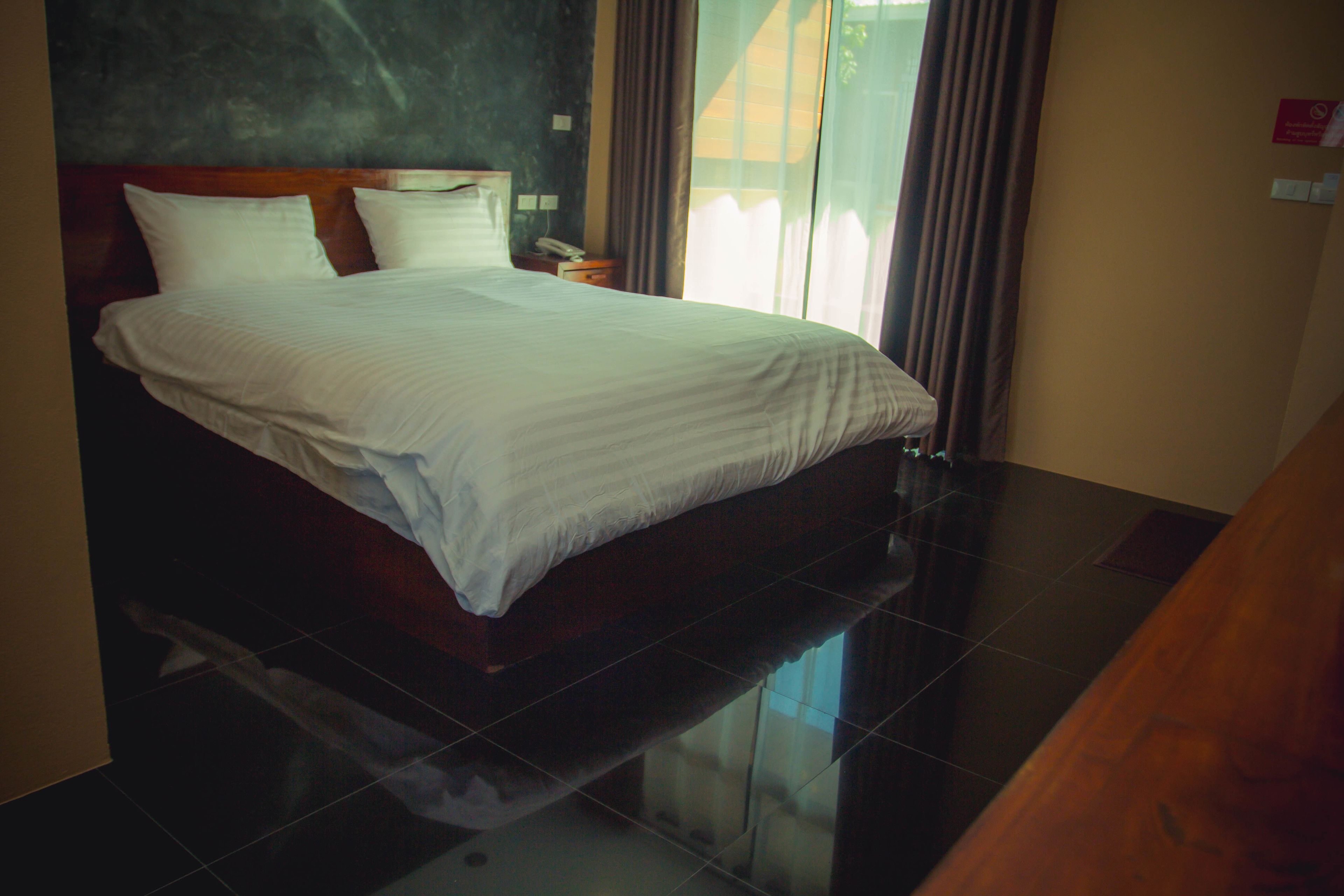 A hotel room with a large bed, a nightstand, and a view of the outdoors through a window.