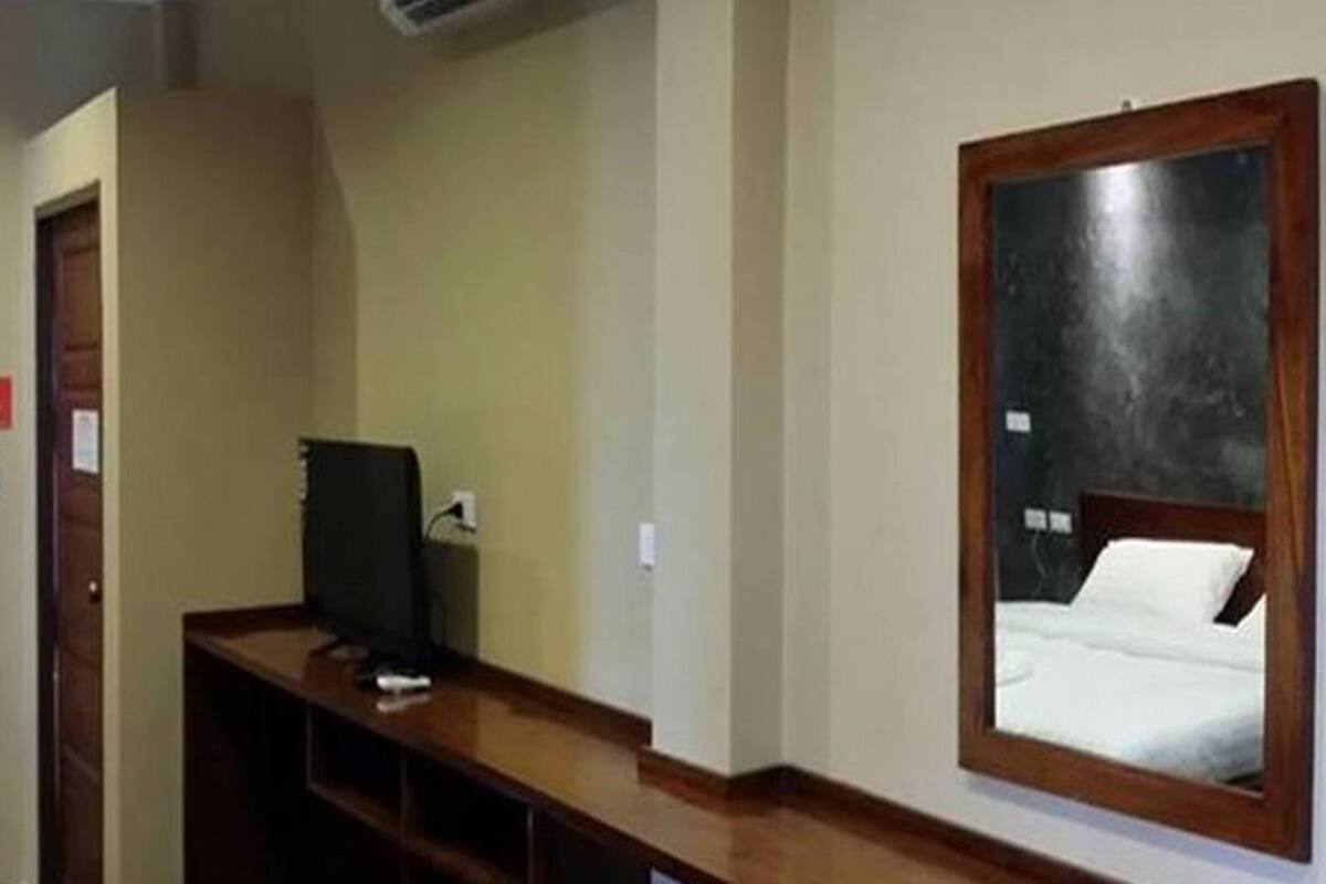Een hotelkamer met een houten bureau, een computer, een bed met een witte matras en een spiegel aan de muur.
