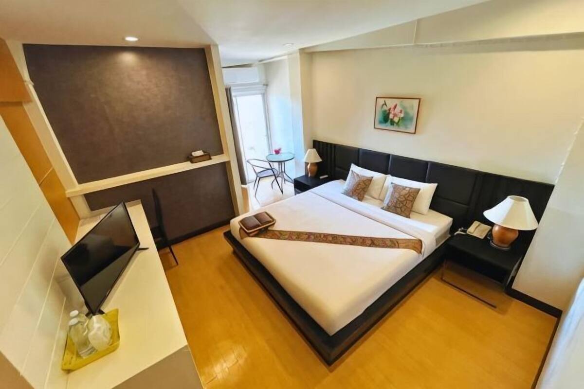 Ein Hotelzimmer mit Bett, Nachttisch, Lampe und Schreibtisch mit Computer.