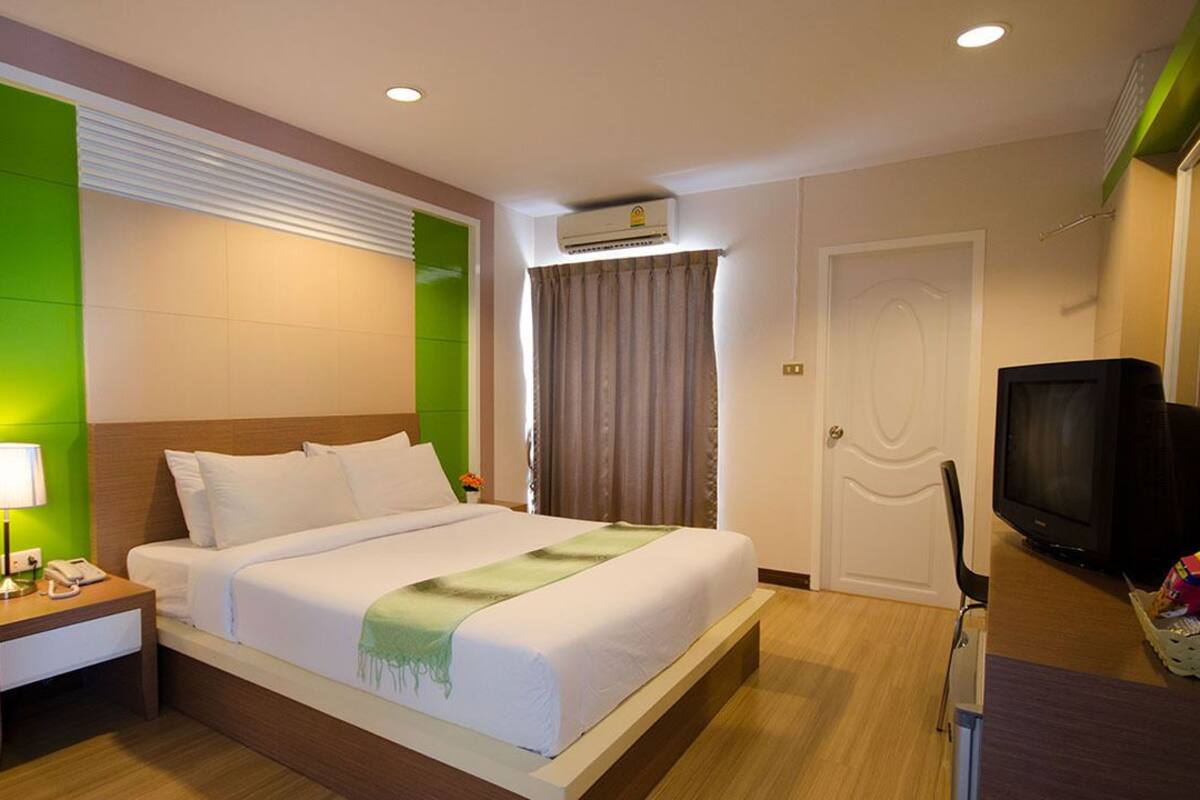 Ein Hotelzimmer mit Bett, Nachttisch, Lampe, Klimaanlage, Fernseher und einem kleinen Tisch mit Snacks.