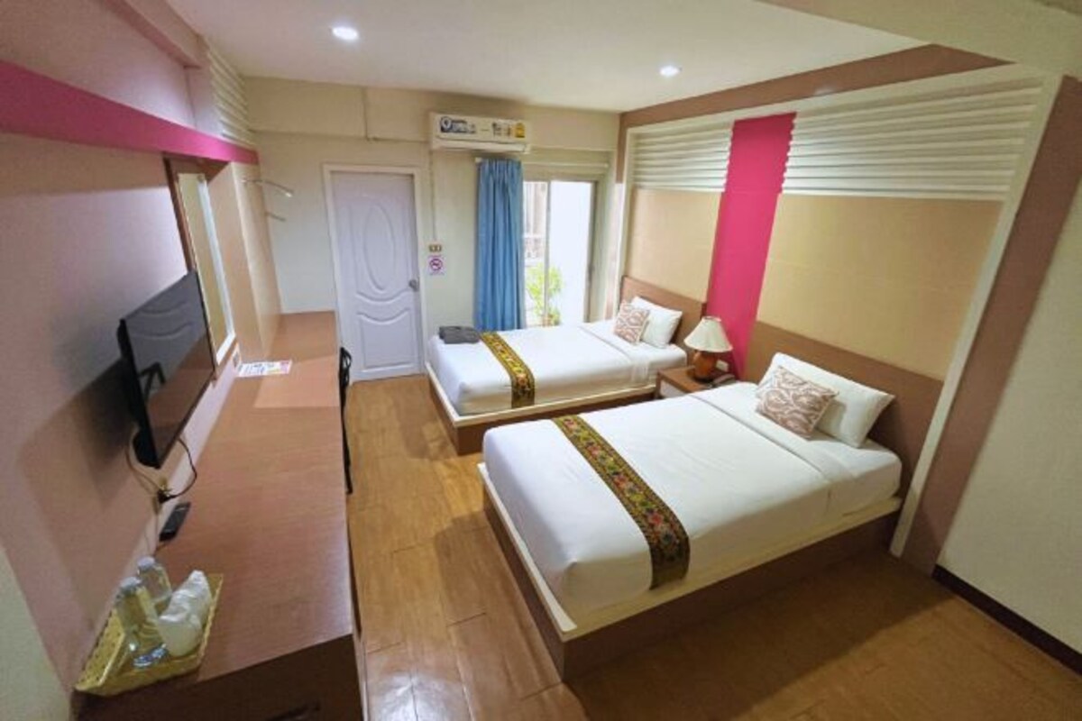 A hotel room with two beds, a desk, a television, and a window with curtains.