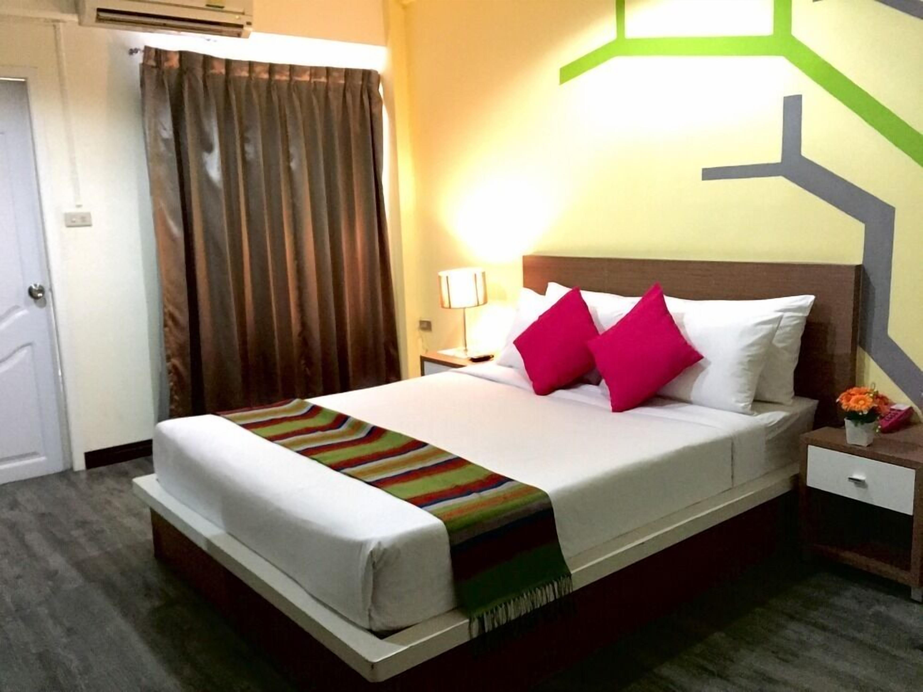 A hotel room with a bed, a nightstand, a lamp, and a curtain.