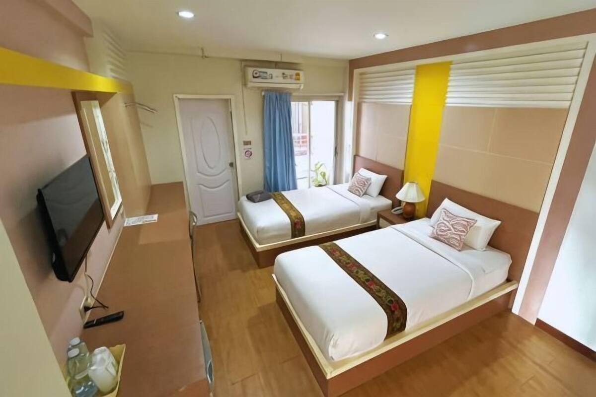 Ein Hotelzimmer mit zwei Betten, einem Fernseher, einem Badezimmer und einem Fenster mit Vorhängen.
