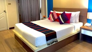 Quarto de hotel com cama, mesa de cabeceira, luminária e janela com cortinas.