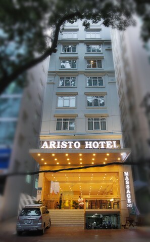 L’extérieur de l’hôtel Aristo, avec une entrée bien visible, une voiture garée devant et un panneau indiquant un service de massage.
