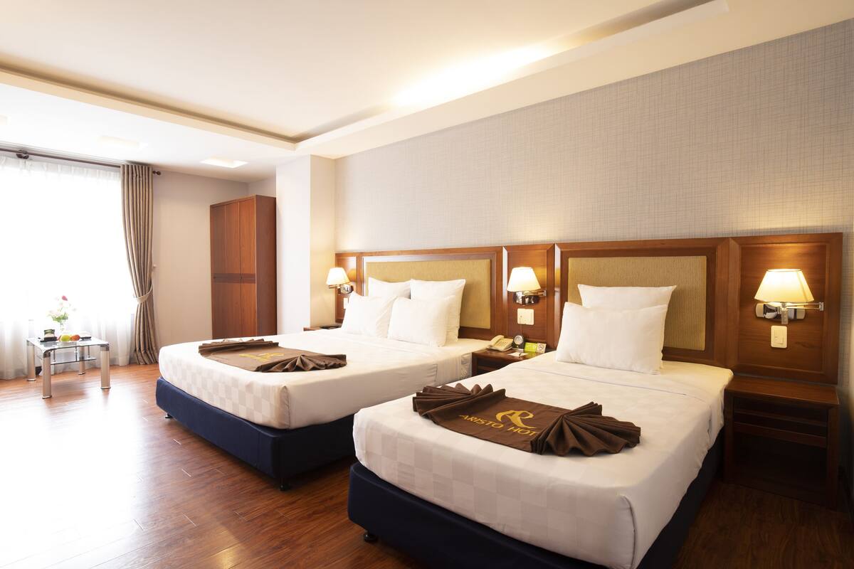 Une chambre d’hôtel avec deux lits, une tête de lit en bois, des lampes de chevet et une petite table avec une lampe.