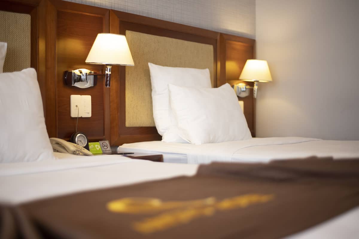 Une chambre d’hôtel avec deux lits, chacun doté de draps blancs, d’une tête de lit en bois et d’une lampe fixée au mur.