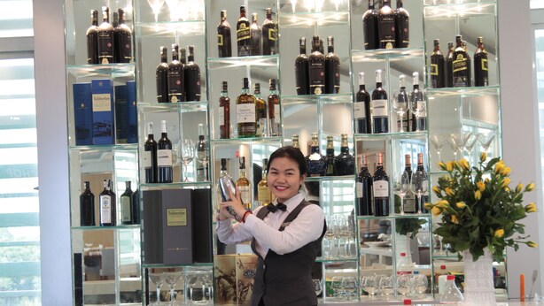 Un espace bar avec un barman tenant une bouteille, entouré d’étagères remplies de différentes bouteilles d’alcool et de verres.