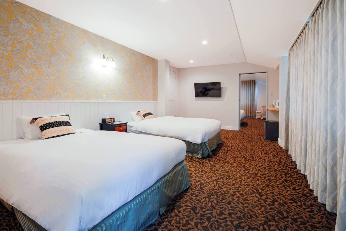 A hotel room with two beds, a carpeted floor, a painting on the wall, and a bathroom visible through an open door.