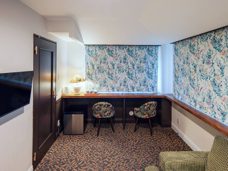 A corner room with a desk, two chairs, a TV, and a patterned carpet.