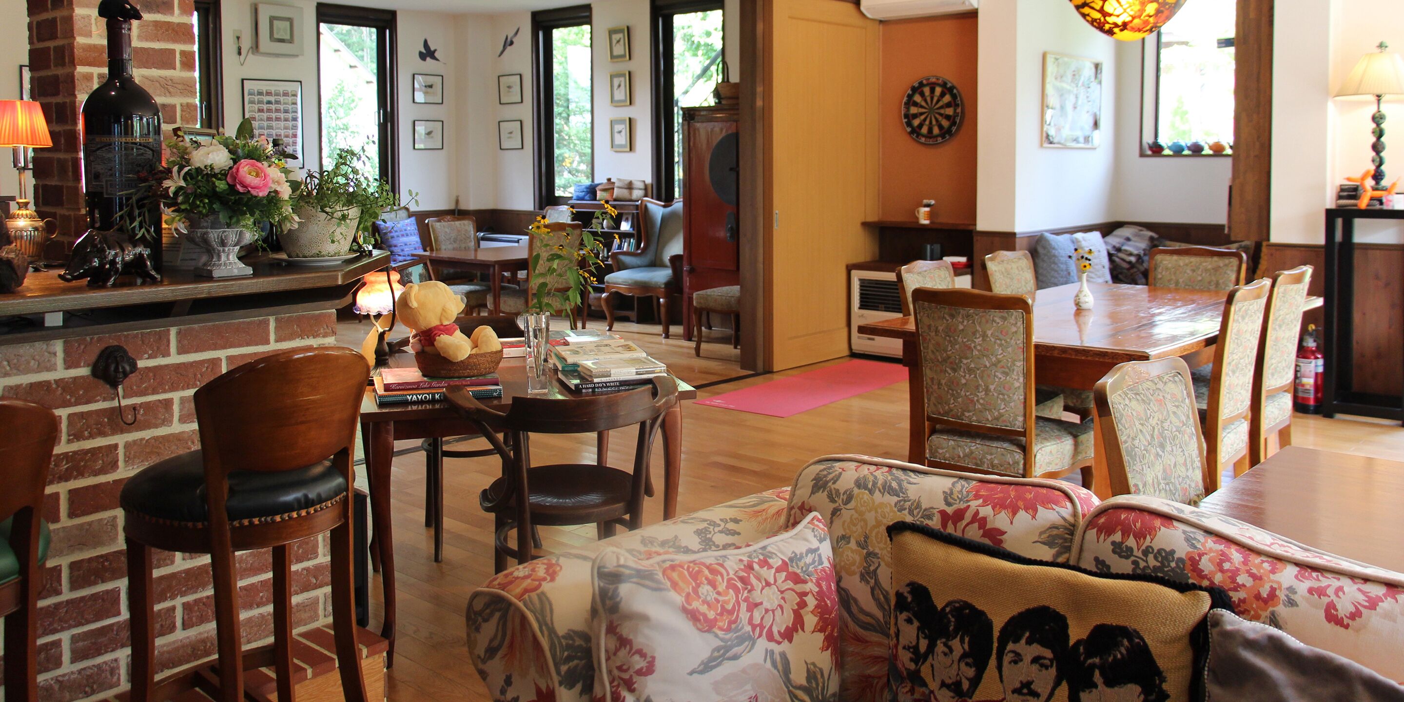 A cozy living room with a brick fireplace, a dining area with a wooden table and chairs, and a comfortable seating area with floral cushions.