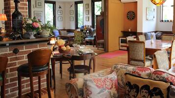 A cozy living room with a brick fireplace, a dining area with a wooden table and chairs, and a comfortable seating area with floral cushions.