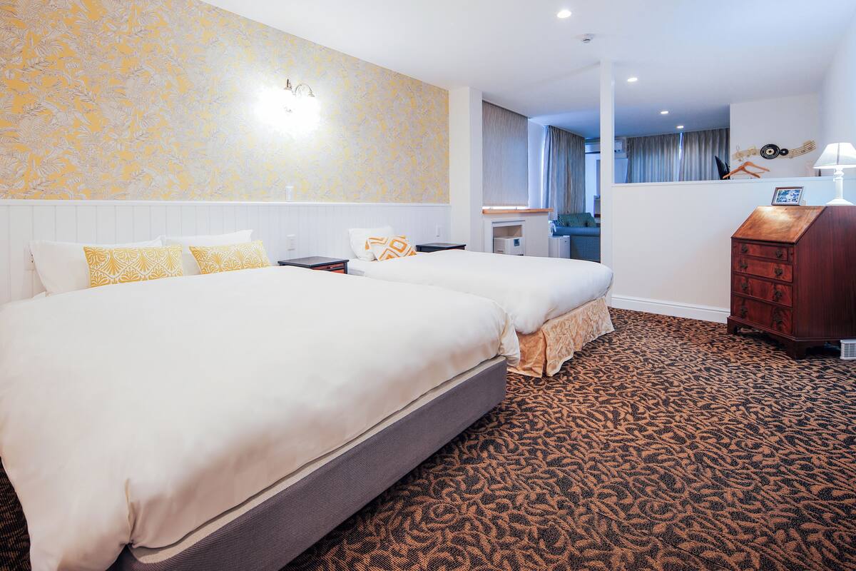 A hotel room with two beds, a wooden dresser, a desk, and a patterned carpet.