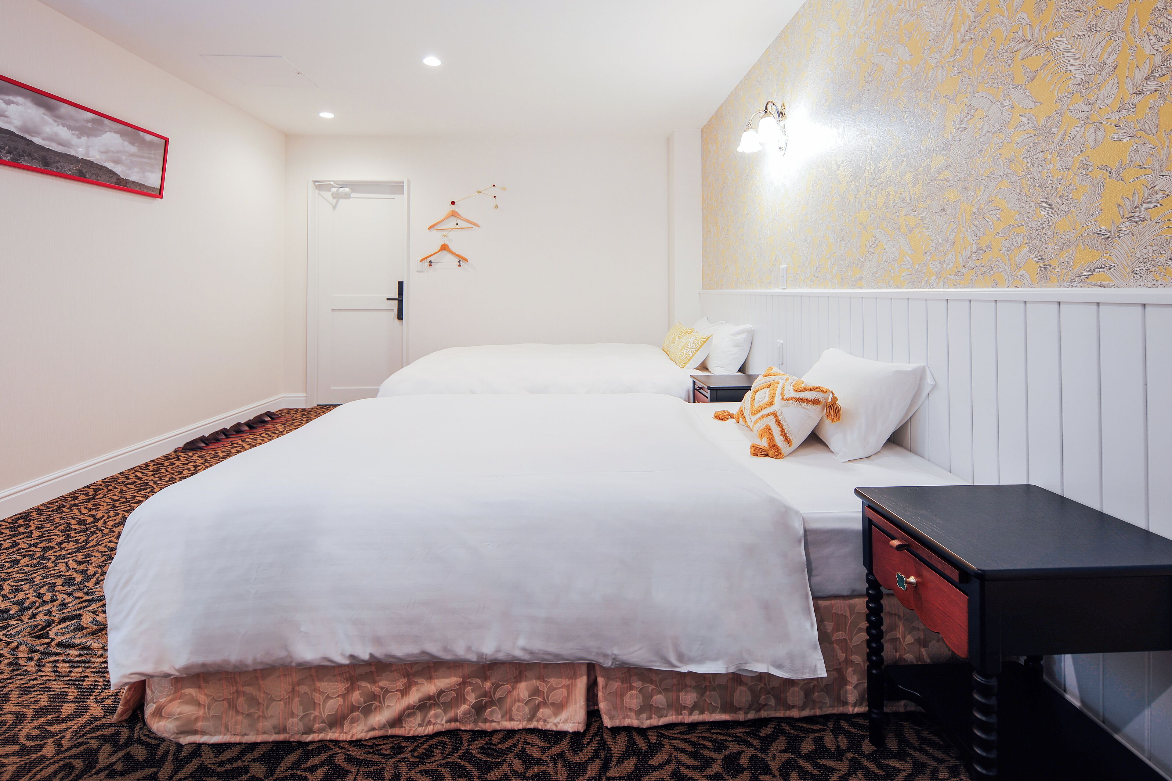 Une chambre d’hôtel avec deux lits, un petit bureau et une moquette à motifs.