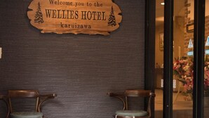 A wooden sign welcoming guests to the WELLIES HOTEL in Karuizawa, with two wooden chairs and a small table in front. - Hotel WELLIES (Karuizawa)