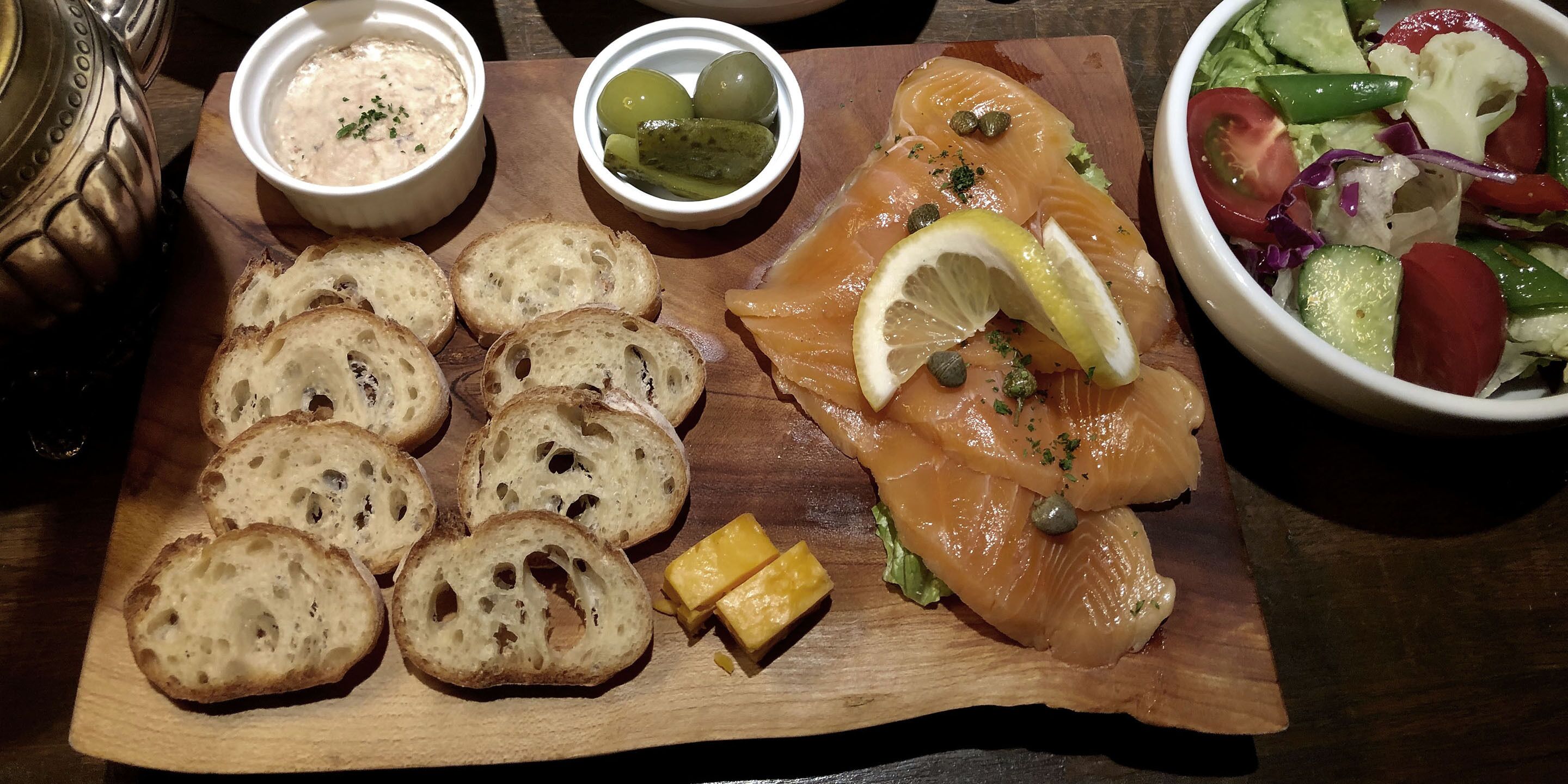 Ein Holzbrett mit Brot, Räucherlachs, Zitrone, Kapern und Käse.