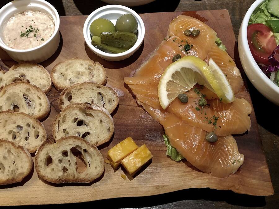 Ein Holzbrett mit Brot, Räucherlachs, Zitrone, Kapern und Käse.