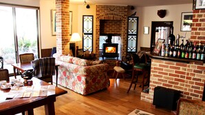 A cozy living room with a fireplace, a dining area, and a bar with a variety of bottles. - Hotel WELLIES (Karuizawa)